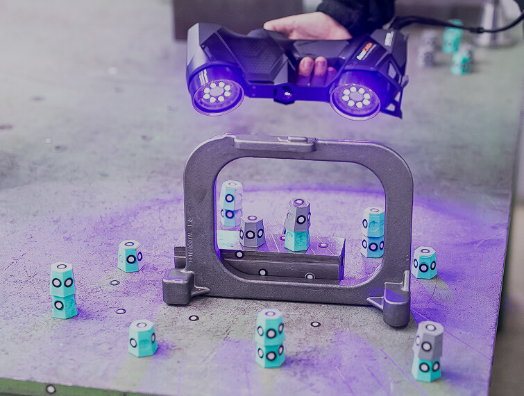 Dispositivo de escaneo 3D capturando datos de una pieza metálica con marcadores de referencia
