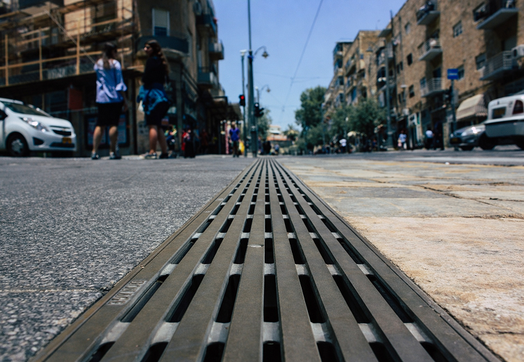 Primer plano de una rejilla de alcantarillado en una calle urbana con peatones